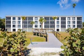 Un edificio moderno con varios balcones, una terraza de madera y palmeras.