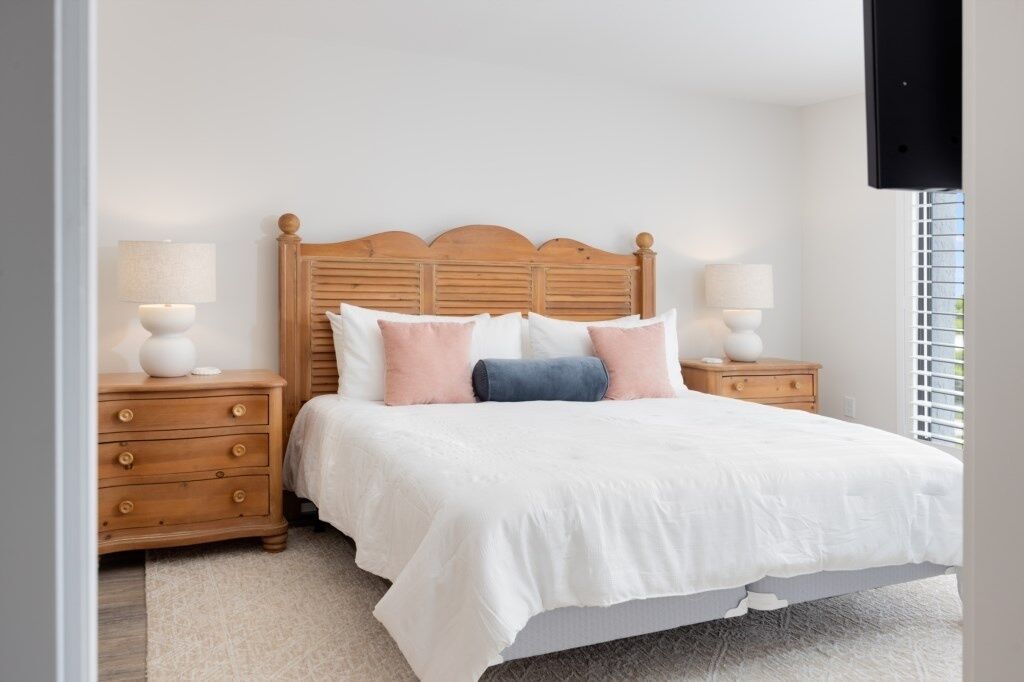 A bedroom with a wooden headboard, a white bedspread, and two bedside tables with lamps.