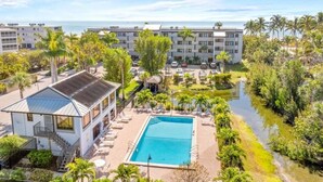 A resort with a swimming pool, palm trees, and a view of the ocean. - Pelicans Roost 105 2 Bedroom Condo (Sanibel)