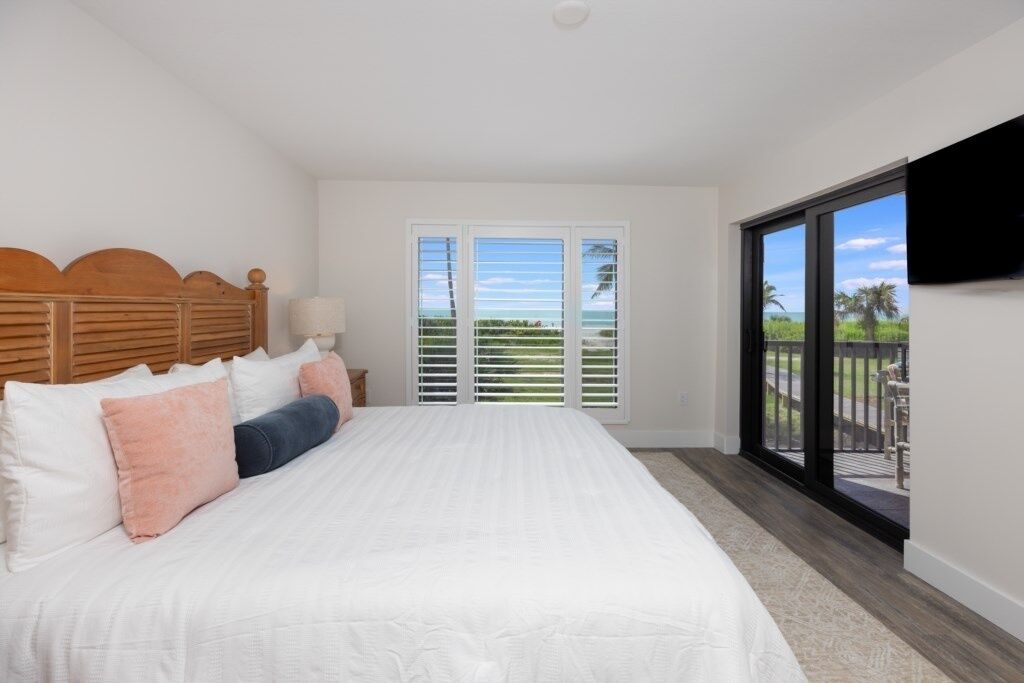 A bedroom with a large bed, white bedding, a wooden headboard, and a view of the outdoors through a sliding glass door.