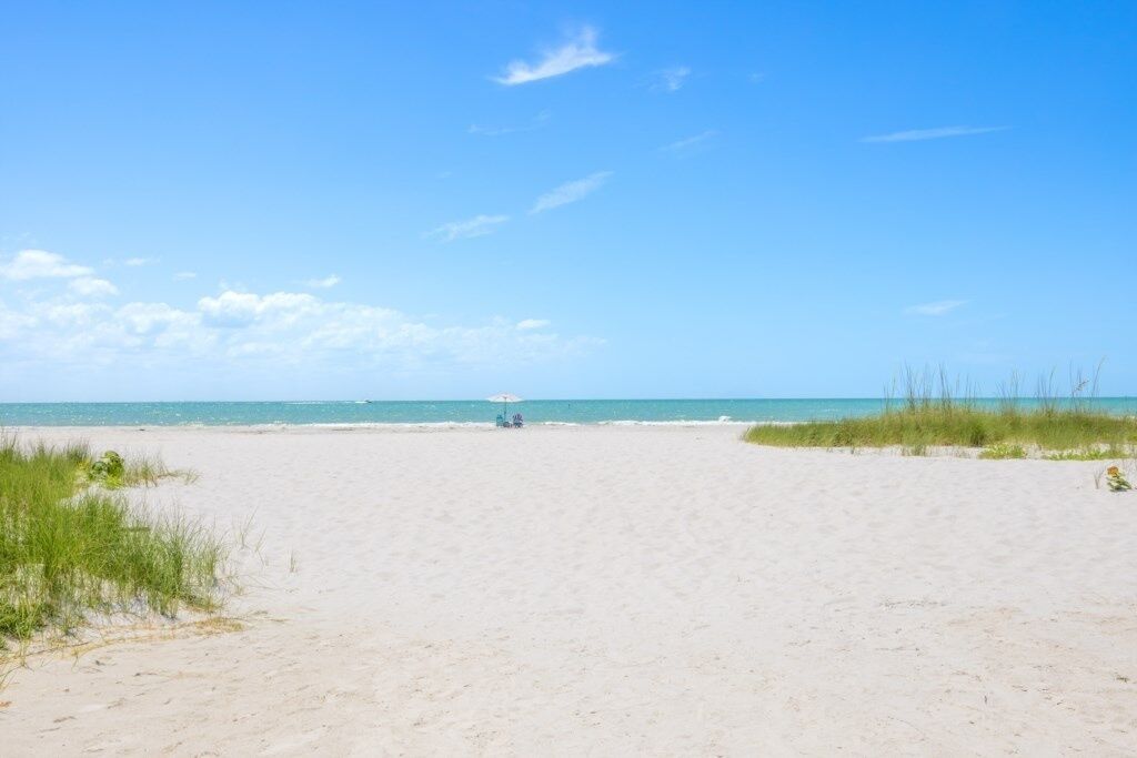 En bred, sandet strand med en klarblå himmel og roligt hav.