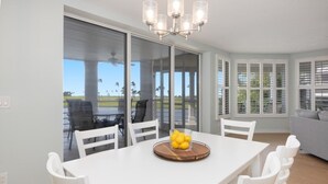 A dining area with a white table, white chairs, and a chandelier. - Captivated By The Sea 2 Bedroom Condo (Captiva)