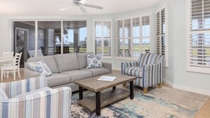 A spacious living room with a grey sofa, striped armchairs, a wooden coffee table, and a ceiling fan. - Captivated By The Sea 2 Bedroom Condo (Captiva)