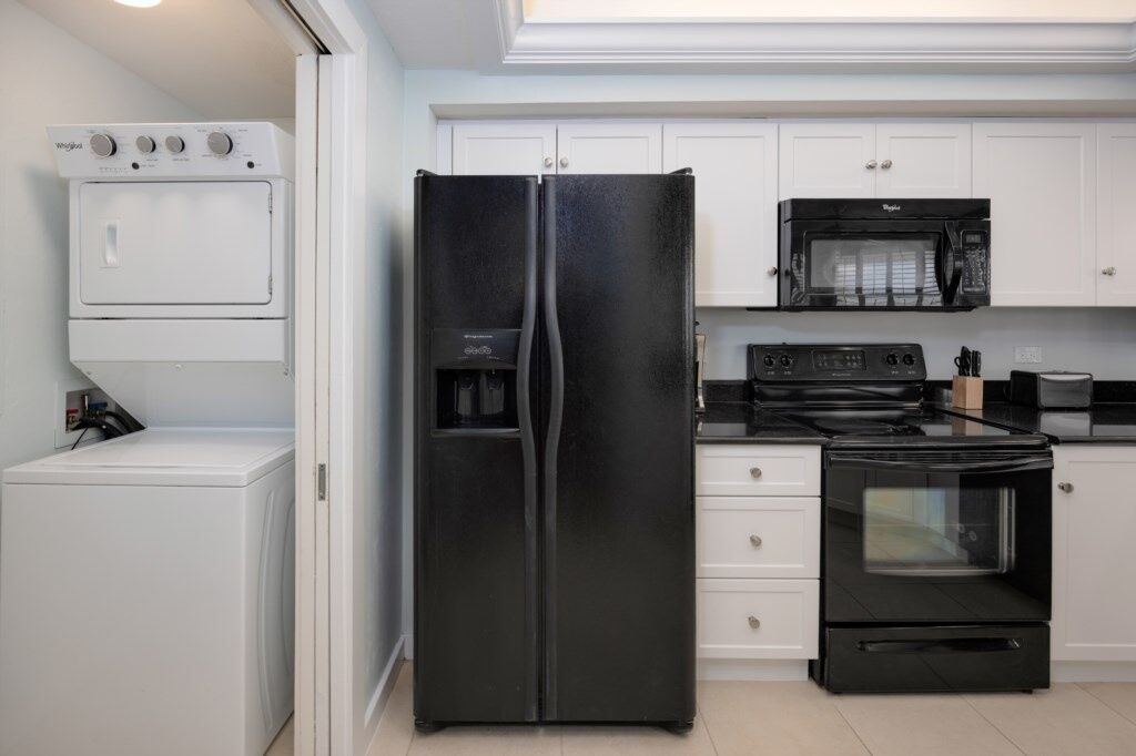 A kitchen with a black refrigerator, a microwave, a stove, and a washing machine.