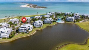 An aerial view of a coastal resort with multiple buildings, a large body of water, and a distant island. - Captivated By The Sea 2 Bedroom Condo (Captiva)
