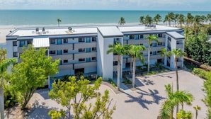 A multi-story hotel with a rooftop pool, surrounded by palm trees and a beach view. - Pelicans Roost 305 2 Bedroom Condo (Sanibel)
