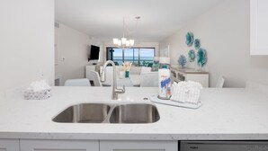 A modern kitchen with a double sink, stainless steel faucet, and a white countertop. - Pelicans Roost 305 2 Bedroom Condo (Sanibel)