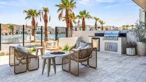 A rooftop patio with wicker furniture, a grill, and a view of a swimming pool and buildings. - Rosemary 7 Bedroom Home (St. George)