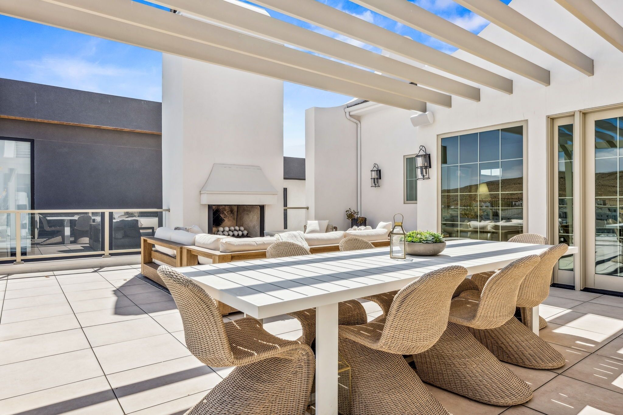 A rooftop patio with a white table and wicker chairs, a sofa set, and a fireplace.