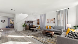 A modern living room with a grey sofa, coffee table, and a dining area with a table and chairs. - World Showcase At Windwood Bay By Shine Villas 5 Bedroom Villa (Davenport)