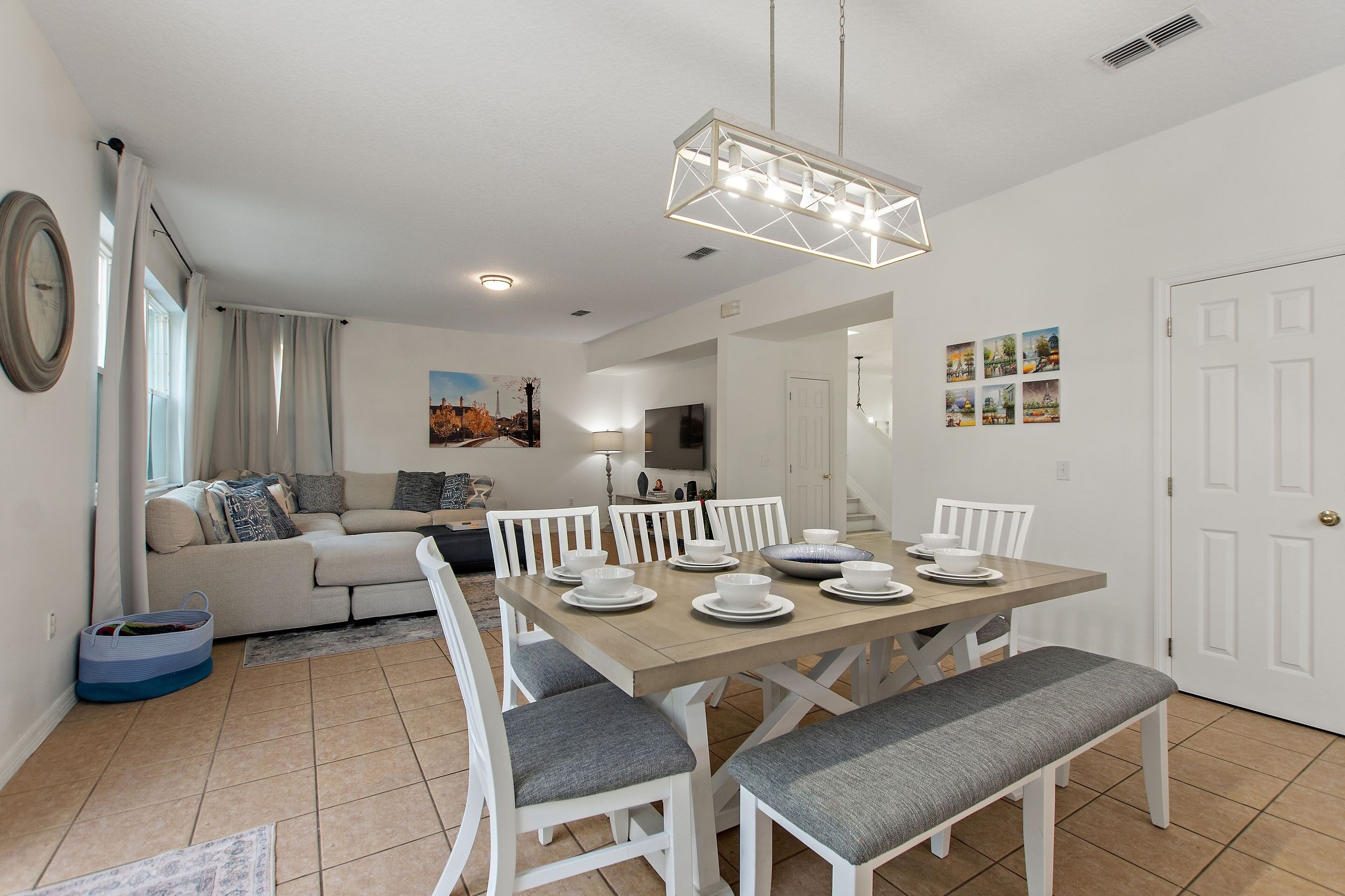 A dining area with a wooden table set for four, surrounded by white chairs with grey cushions.
