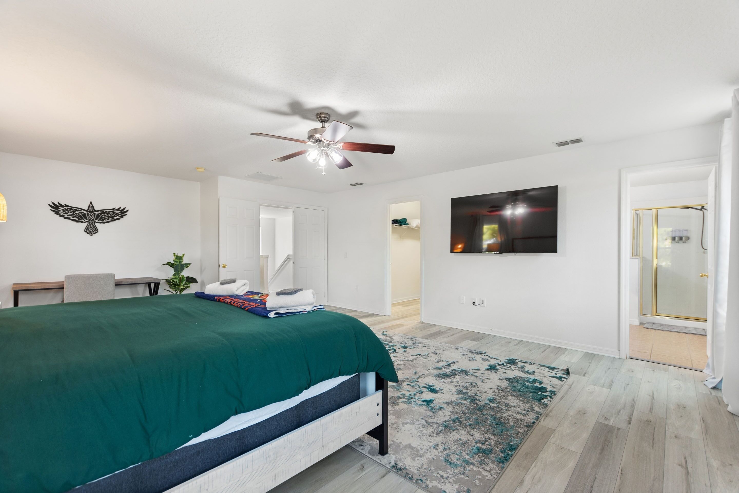 A bedroom with a bed, a ceiling fan, a TV mounted on the wall, and a door leading to a bathroom.