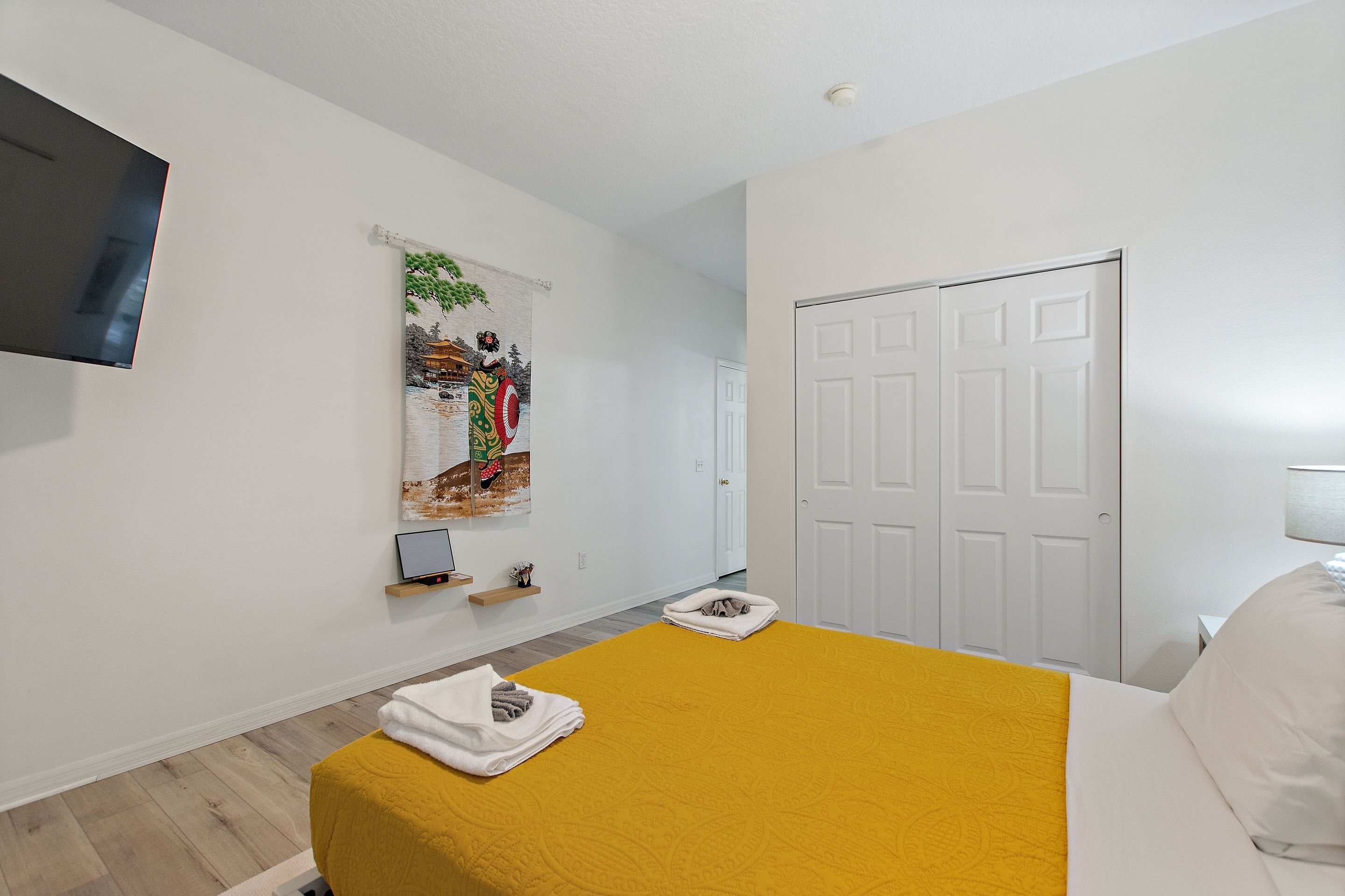 A hotel room with a bed, a TV mounted on the wall, a door, and a window with a curtain.