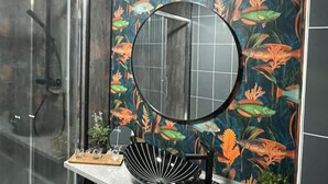 A bathroom with a round mirror, a black fan, and a decorative wall with a fish and plant pattern. - The Exclusive Jacuzzi Apartment (Birmingham)