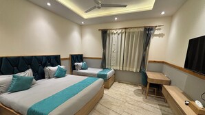 A hotel room with two beds, a desk, a chair, a ceiling fan, and a TV mounted on the wall.