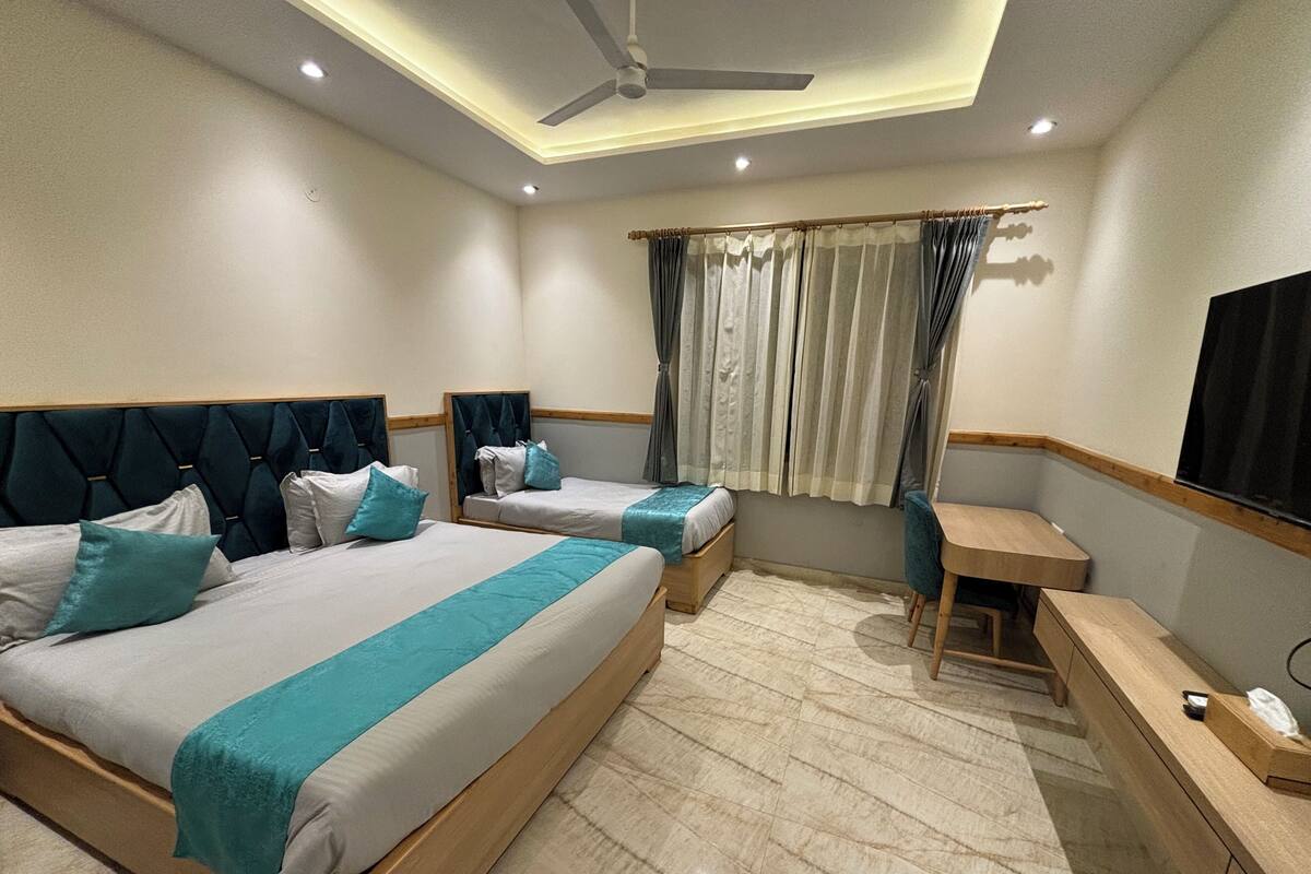 Habitación de hotel con dos camas, un escritorio, una silla, un ventilador de techo y un televisor montado en la pared.