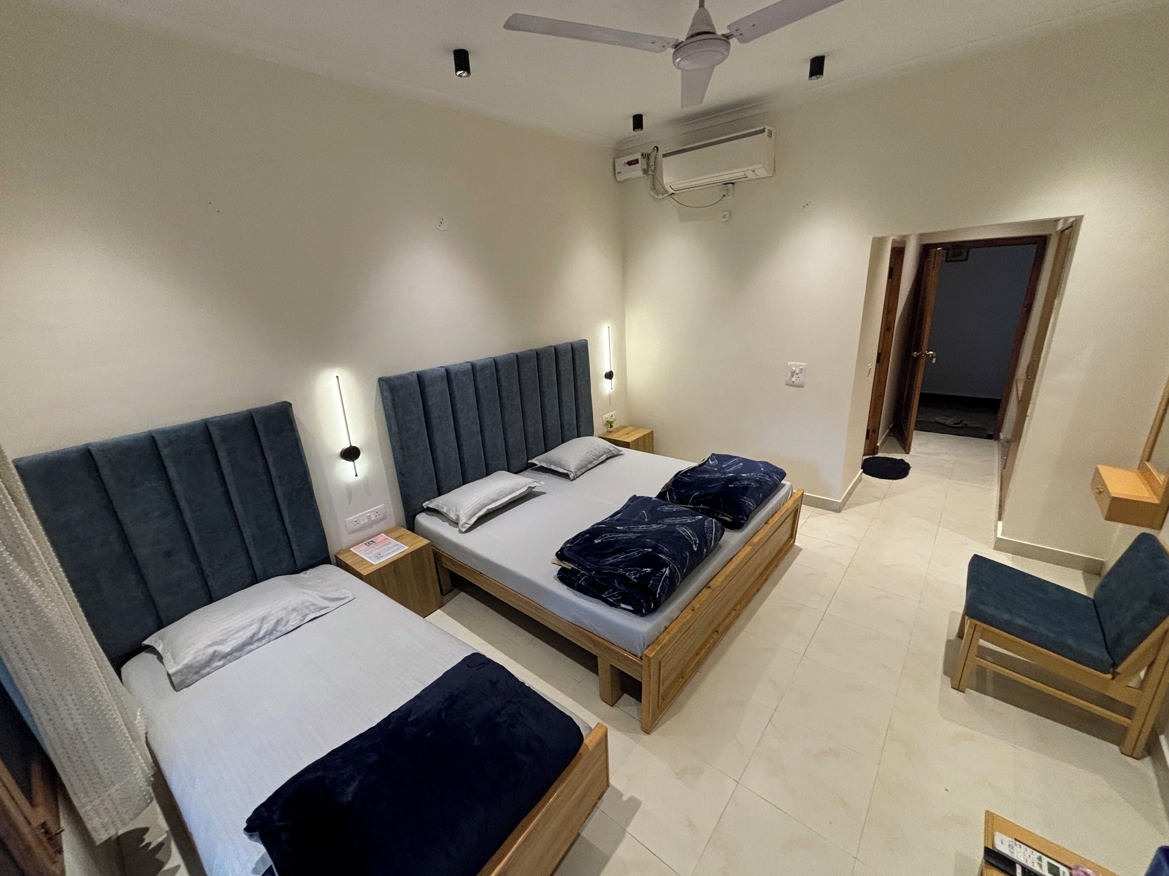 Habitación de hotel con dos camas, un ventilador de techo, un equipo de aire acondicionado y una pequeña silla de madera.