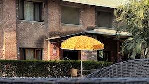 A brick building with a pool reflecting an umbrella and chairs.