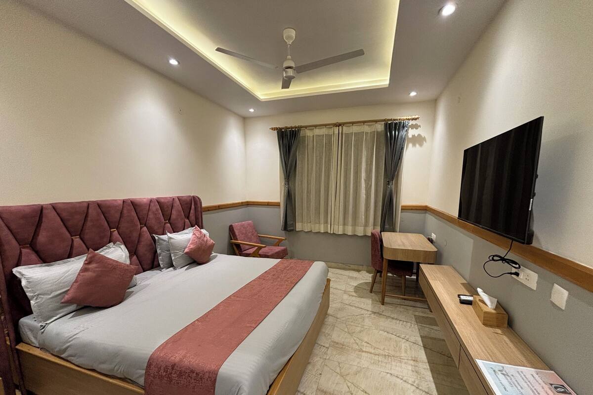 Habitación de hotel moderna con una cama grande, un escritorio, una silla, un televisor de pantalla plana y un ventilador de techo.