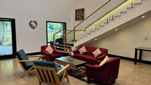 A spacious living area with a red sofa set, a wooden armchair, and a coffee table. A staircase with a glass railing leads to an upper level.