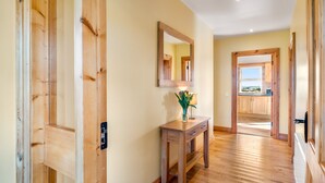 A hallway with wooden flooring, a wooden console table with a lamp and vase, and a mirror on the wall.