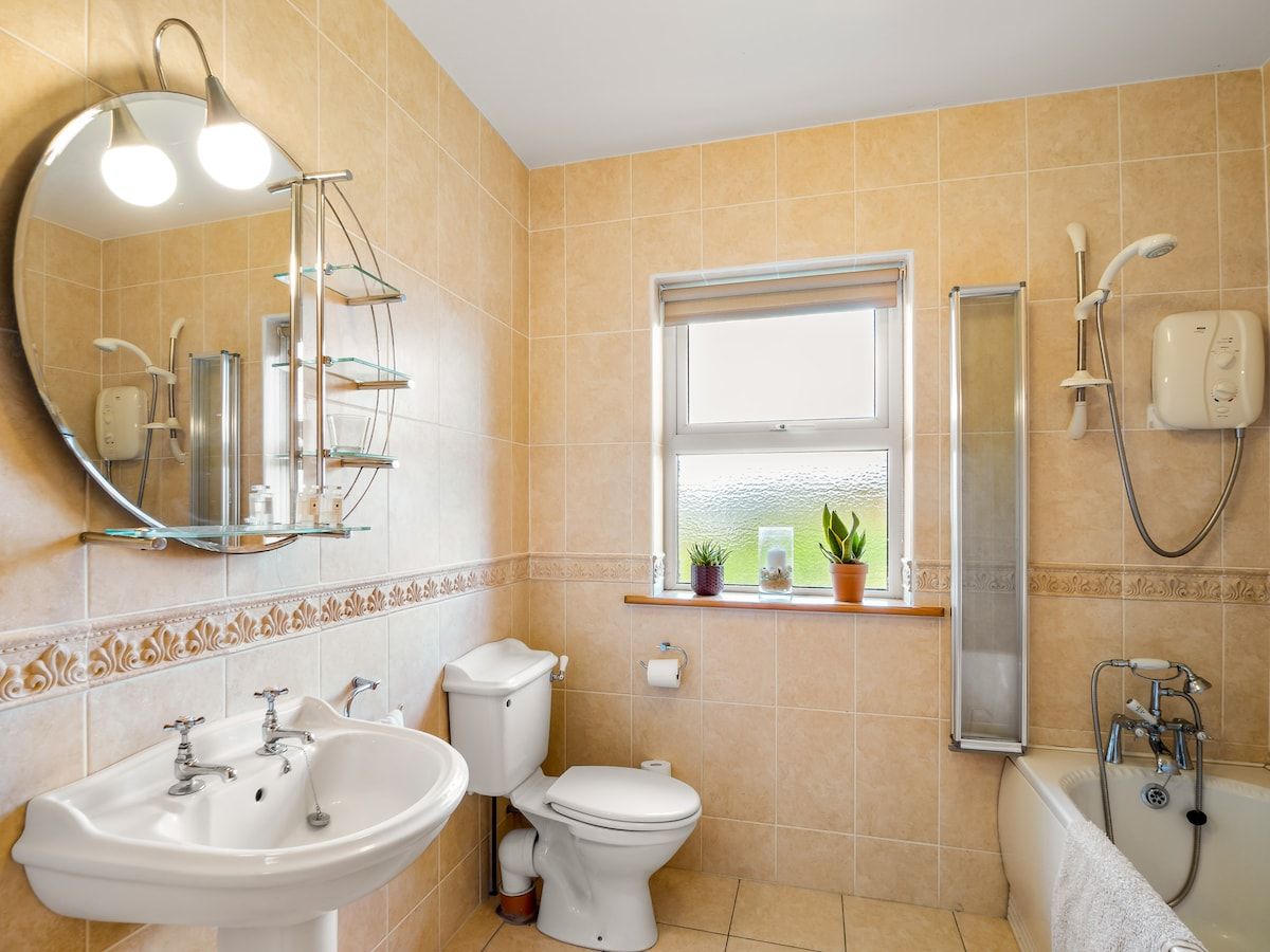 Un baño con lavabo, inodoro y bañera. Hay una ventana con vistas a zonas verdes.
