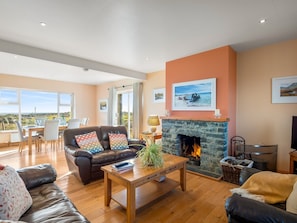 A spacious living room with a fireplace, a dining area with a view, and a sofa with colorful cushions.