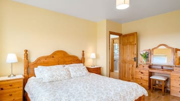 A bedroom with a wooden bed, bedside tables, a desk with a mirror, and a chair.