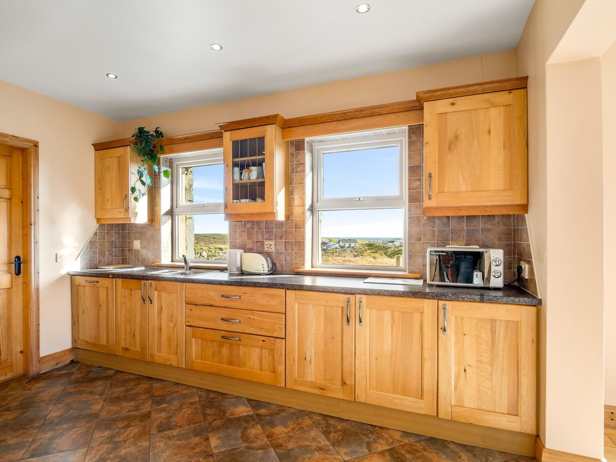 A kitchen with wooden cabinets, a window with a view, and a microwave on the counter.