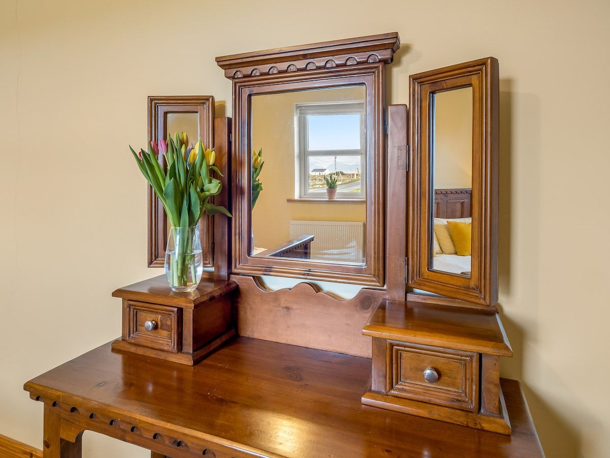A wooden dresser with a mirror and a vase of flowers.