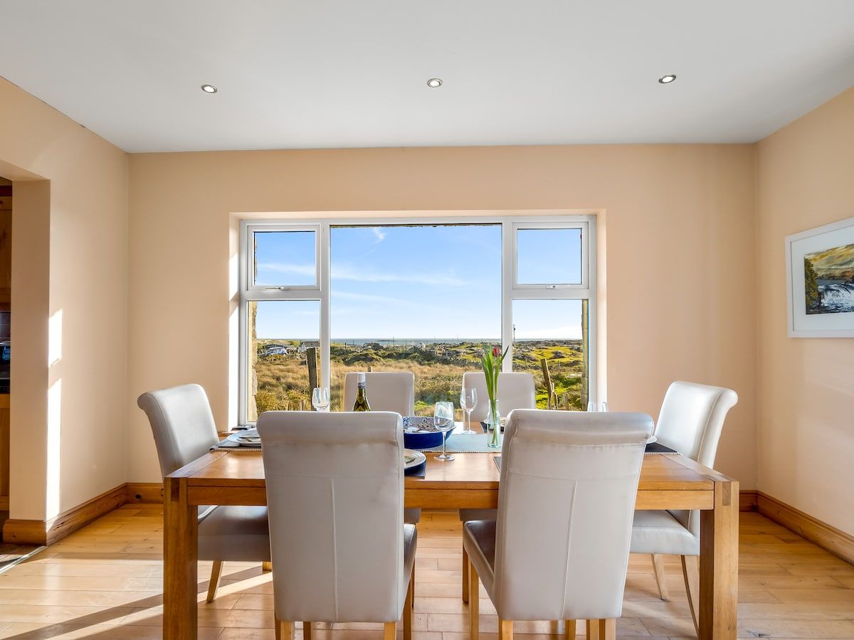 Comedor con una mesa dispuesta para cuatro personas, ventanas amplias y vistas al paisaje.