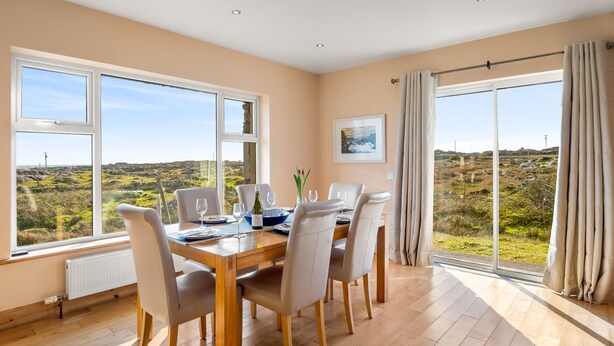 A dining room with a table set for six, large windows offering a view of the countryside, and a single framed picture on the wall.