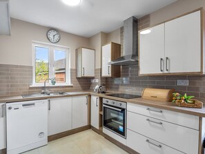 A modern kitchen with white cabinetry, a built-in oven, a sink, and a window with a view of greenery outside.