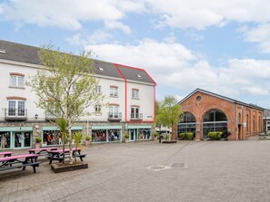 A public square with a building featuring a red roofline and a brick structure with arched windows.