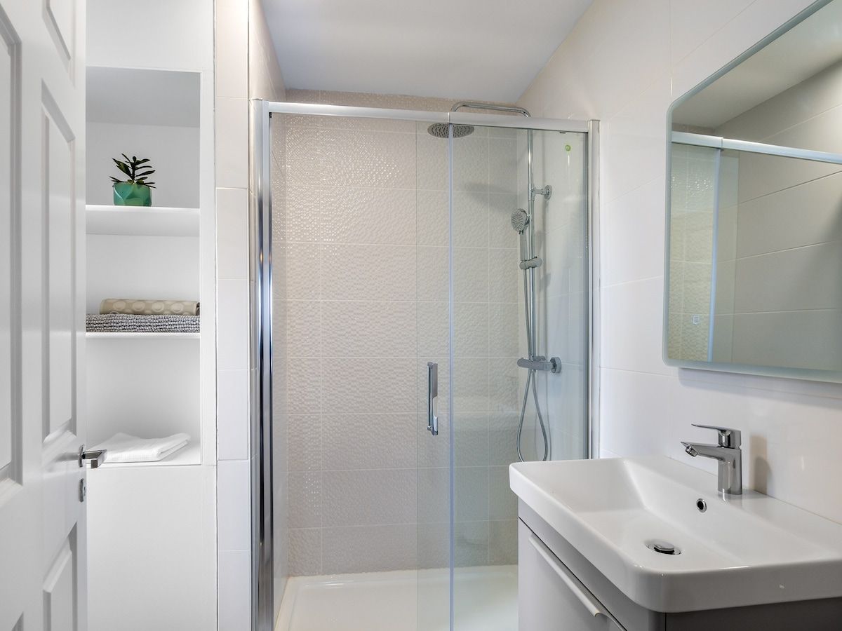 A modern bathroom with a glass-enclosed shower, a white sink, and a mirror above it.