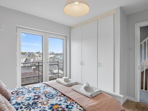 A bedroom with a bed, a large window, and a wardrobe.