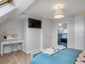A bedroom with a bed, a desk, a chair, a television, and a bathroom visible through an open door.