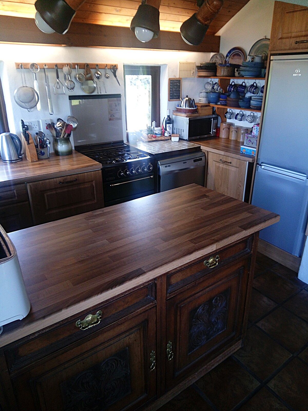 A kitchen with wooden cabinets, a stove, a dishwasher, a microwave, and various kitchen utensils.