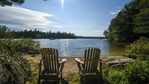 Duas cadeiras Adirondack voltadas para um lago, com uma ilha arborizada ao longe e um céu limpo.
