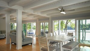 Uma sala de estar ampla com uma mesa de jantar, cadeiras e um sofá. Grandes janelas oferecem vista para o exterior.