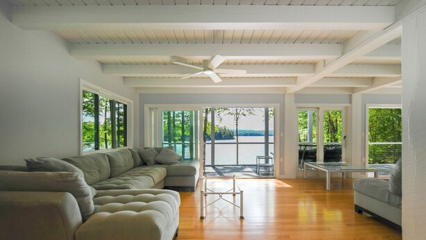 Uma sala de estar ampla com um sofá seccional grande, uma mesa de centro de vidro e um ventilador de teto.