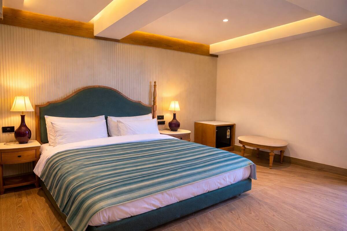 Una camera d'hotel con un letto, due comodini con lampade, un piccolo tavolino in legno e un tavolo rotondo.