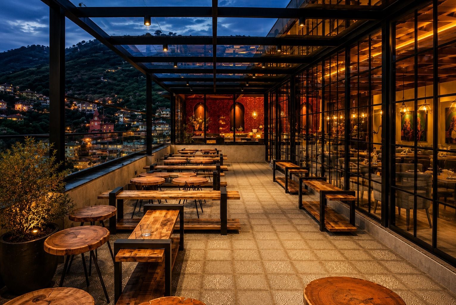 An outdoor terrace with wooden tables and chairs, a patterned floor, and a view of a town and hills in the background.
