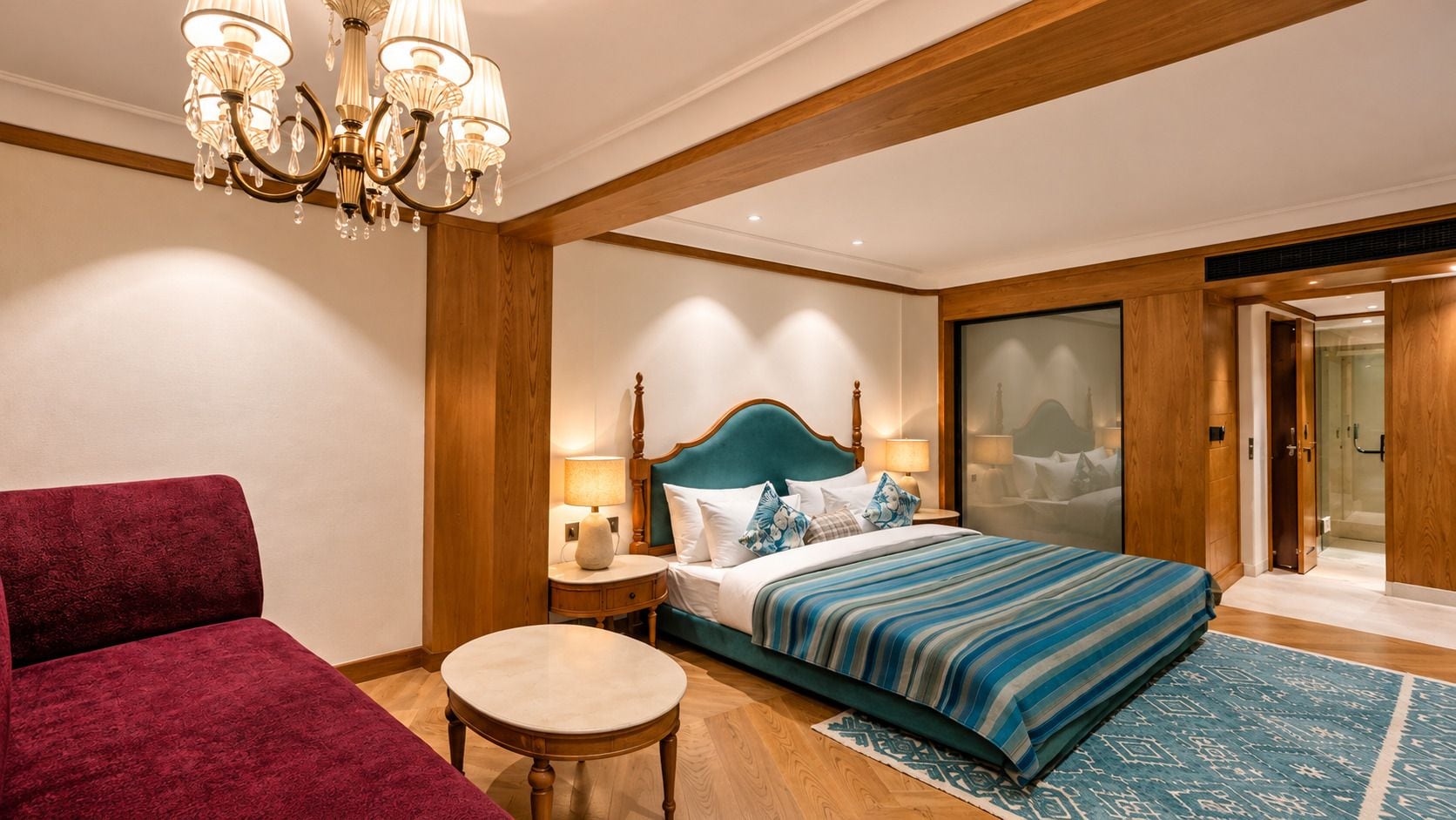 A hotel room with a bed, a red armchair, a round table, and a chandelier.