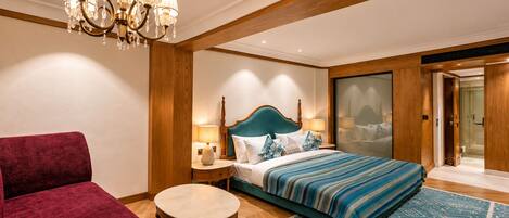 A hotel room with a bed, a red armchair, a round table, and a chandelier.