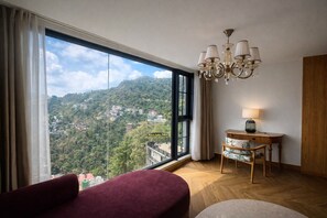 A hotel room with a large window, a chandelier, a small table with a lamp, and a red chair. - AB's Abode-A Boutique Hotel (Mussoorie)