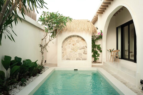 A swimming pool with a stone archway, surrounded by plants and a thatched roof structure.