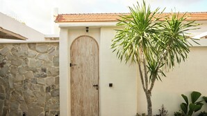 Un muro de piedra, una puerta de madera y una palmera en un patio.
