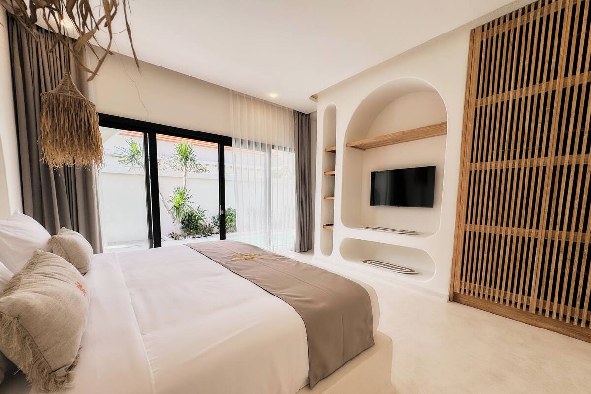 Een moderne slaapkamer met een groot bed, een televisie bevestigd aan een houten paneel en een uitzicht op de omgeving door grote ramen.