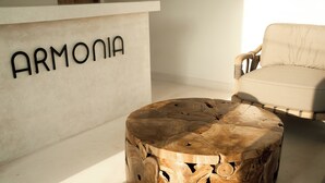 Una mesa redonda de madera con acabado natural, un sofá color beige y una pared con la palabra "ARMONIA" en letras negras.